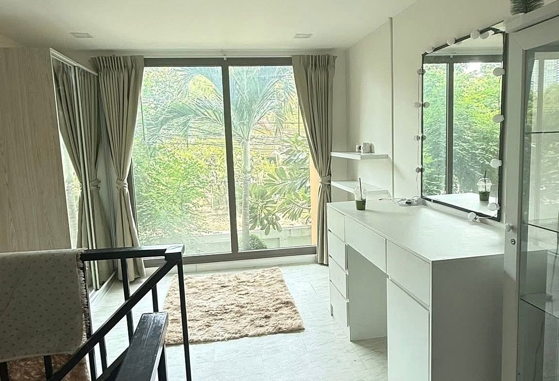 Bright dressing area with a white dresser and illuminated mirror, marble floor, and large window with beige curtains.