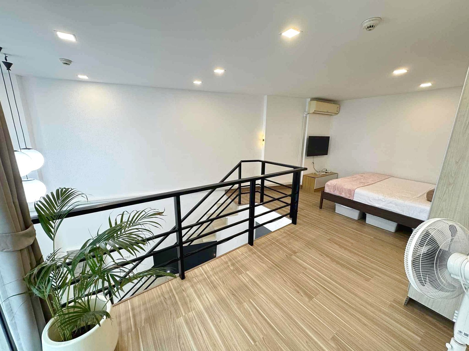 Laguna_Beach_2_Rent_Rdl362_2 Bright loft bedroom with two beds, wall-mounted TV, ceiling lights, and an AC unit; plants near the railing.