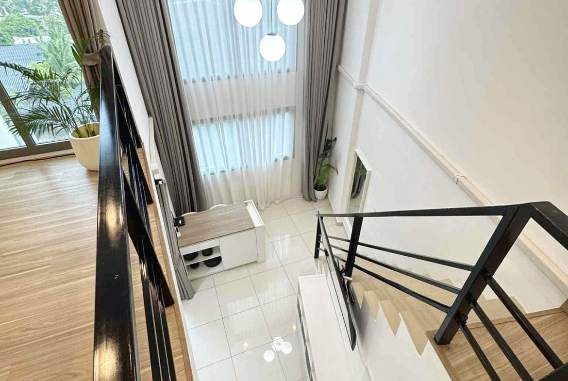 Indoor stairwell from the upper landing, featuring three globe pendant lights, sheer curtains, and potted plants near a window.