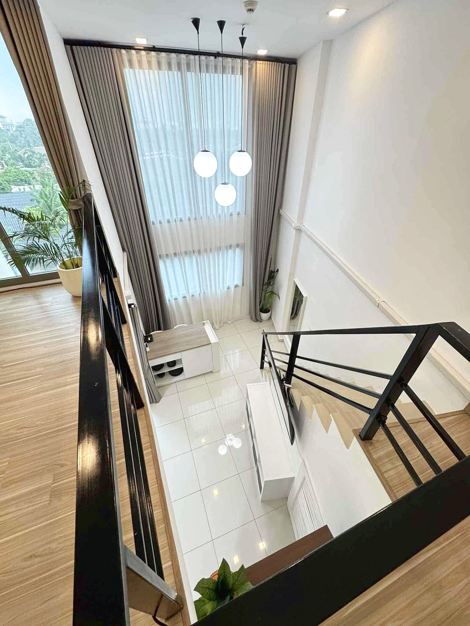 Laguna_Beach_2_Rent_Rdl362_3 Indoor stairwell from the upper landing, featuring three globe pendant lights, sheer curtains, and potted plants near a window.
