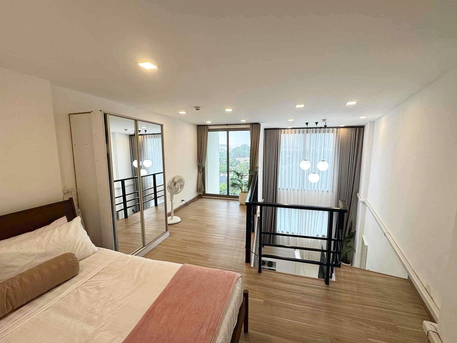 Laguna_Beach_2_Rent_Rdl362_6 Loft bedroom with two single beds in foreground, wooden floor, and glass railing; large windows with sheer curtains in back.
