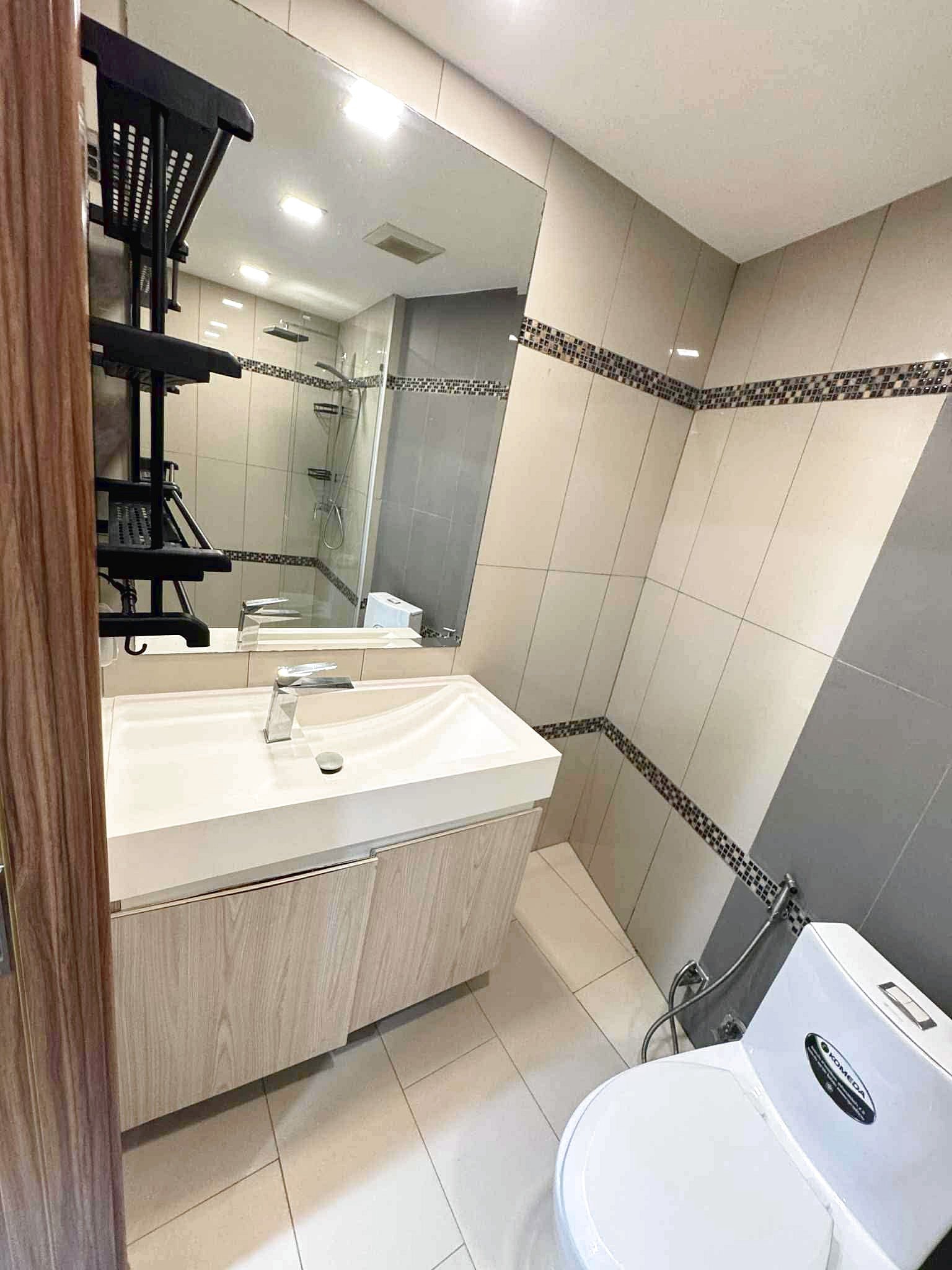 Laguna_Beach_2_Rent_Rdl362_8 Modern bathroom with a white sink vanity, large wall mirror, beige tiled walls, and a glass-enclosed shower; washing machine visible nearby.