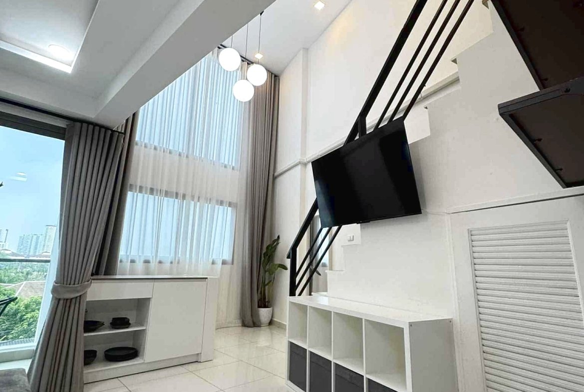 Modern bright living room with white glossy floor, wall-mounted TV, black diagonal staircase, and a potted plant by a cubby shelf.