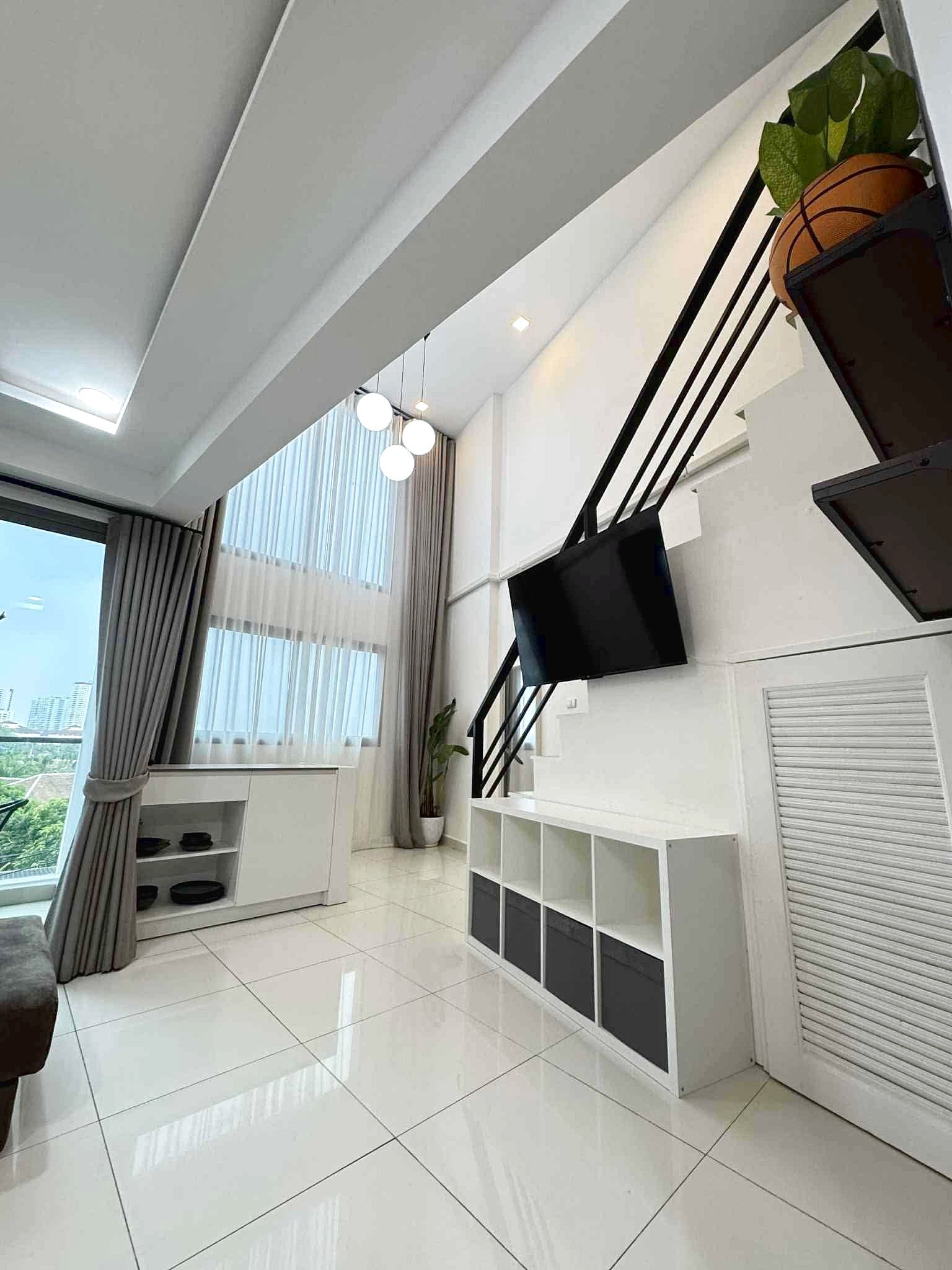 Laguna_Beach_2_Rent_Rdl362_9 Modern bright living room with white glossy floor, wall-mounted TV, black diagonal staircase, and a potted plant by a cubby shelf.