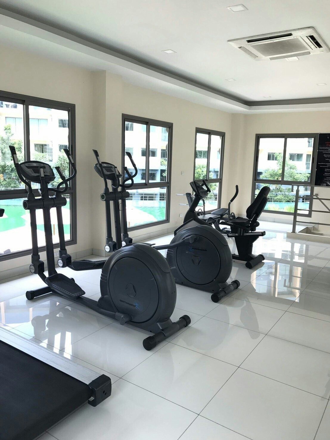Laguna_Beach_Resort_2 37 Bright gym room with cardio machines: two ellipticals, two stationary bikes, and a treadmill by large windows and white tiled floor.