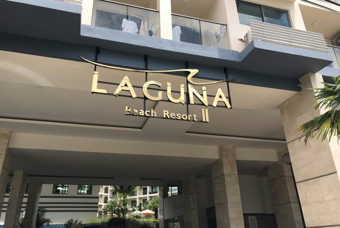 Gold letters spell 'Laguna Beach Resort II' on a modern building entrance canopy, with glass railings above and palm trees nearby.