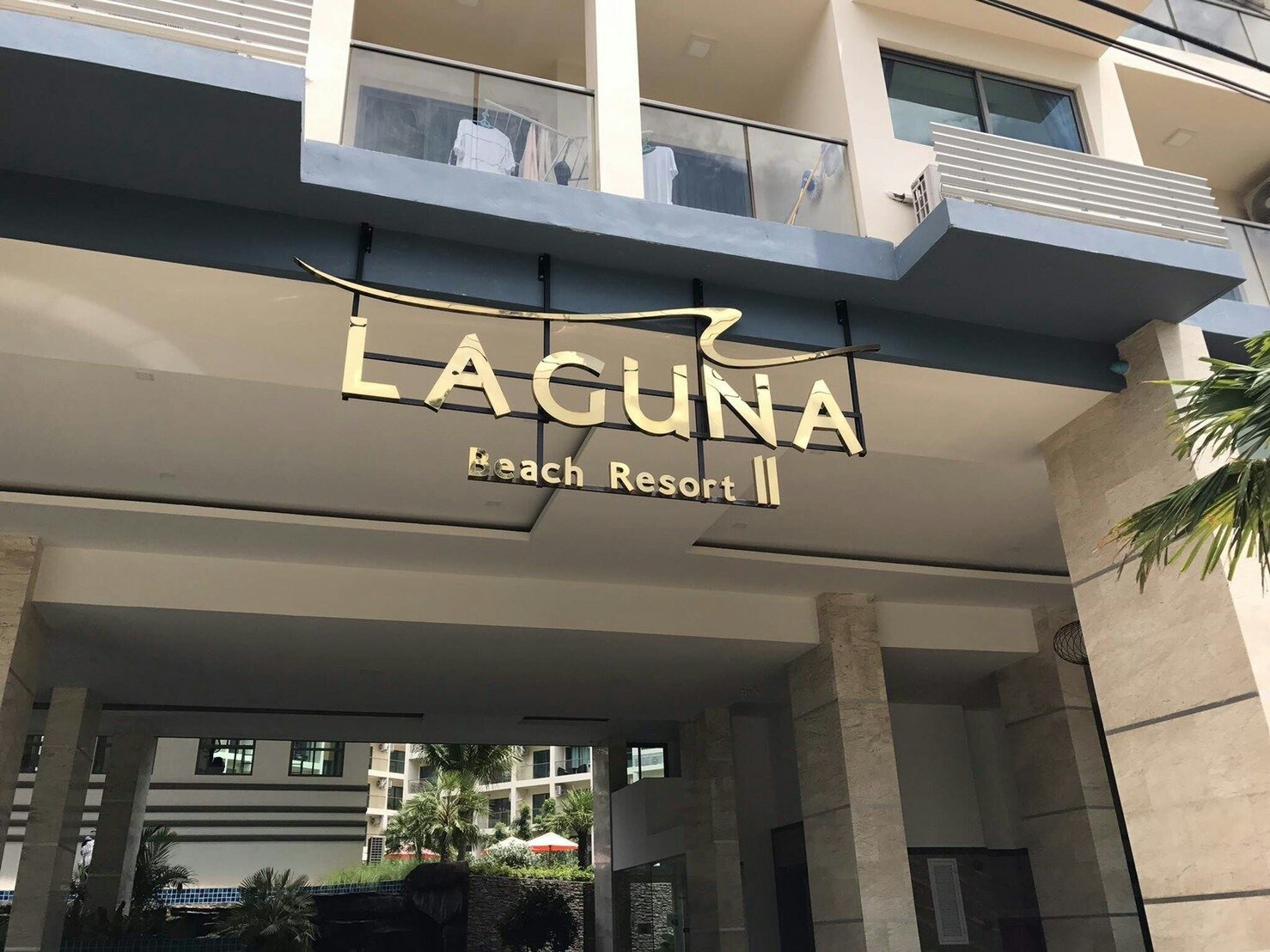 Laguna_Beach_Resort_2 38 Gold letters spell 'Laguna Beach Resort II' on a modern building entrance canopy, with glass railings above and palm trees nearby.