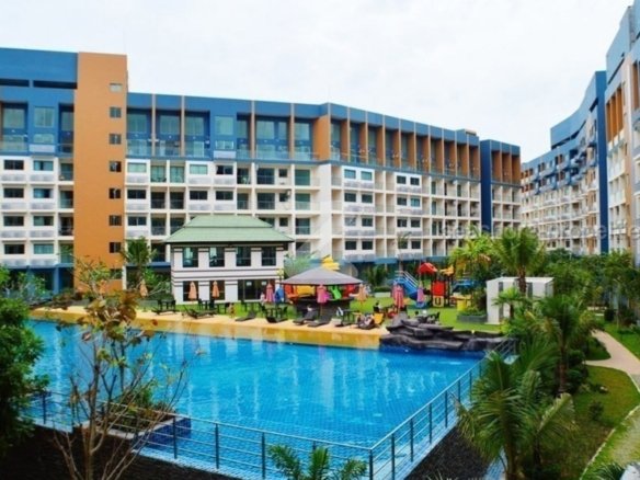 Resort-style hotel courtyard with a large swimming pool, lounge chairs, and colorful buildings surrounding it.