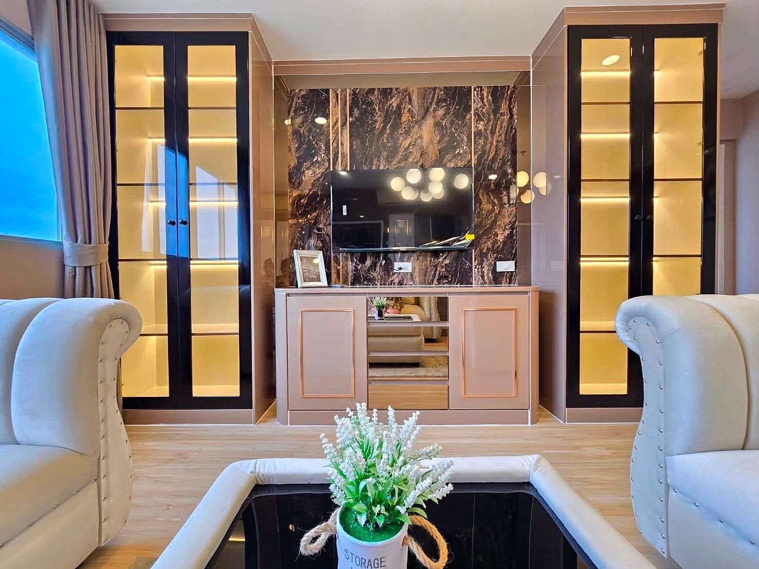 Luxurious living room with a marble feature wall wall mounted TV and beige storage cabinet flanked by tall glass display cabinets