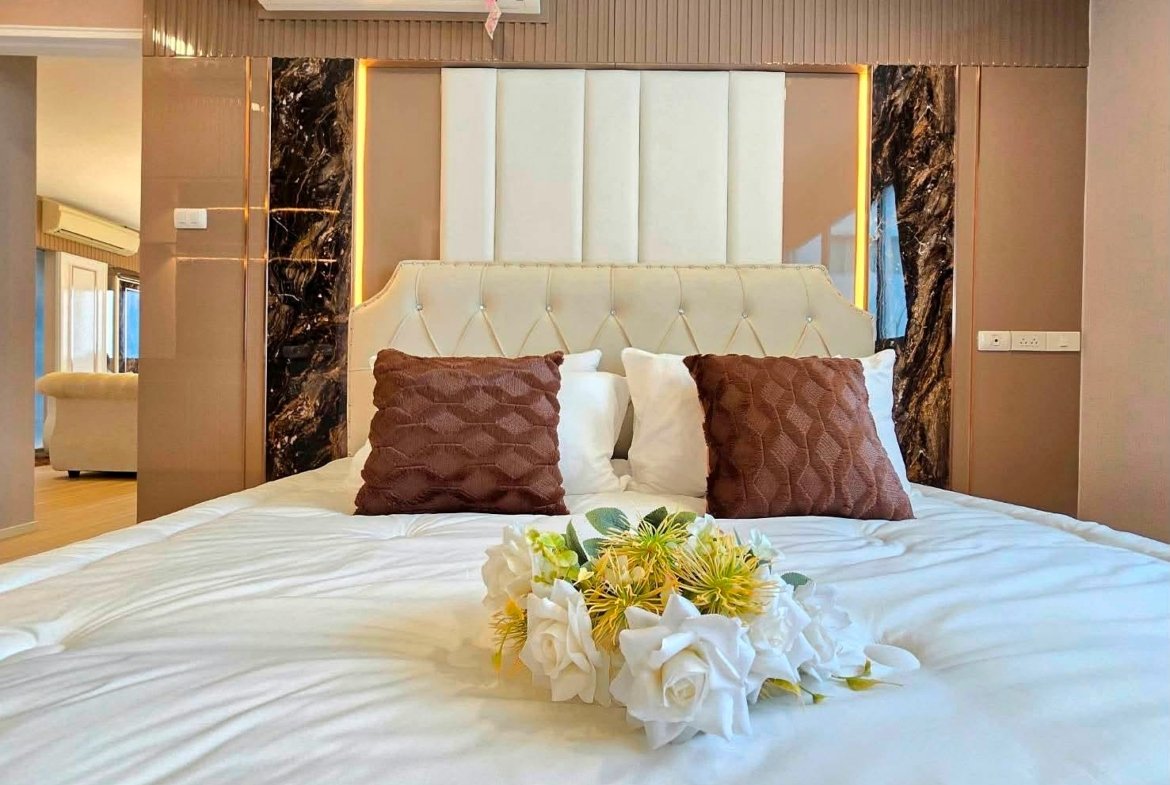 Luxurious bedroom scene with a tufted cream headboard, white sheets, and two brown textured pillows with a floral bouquet in the center of the bed.