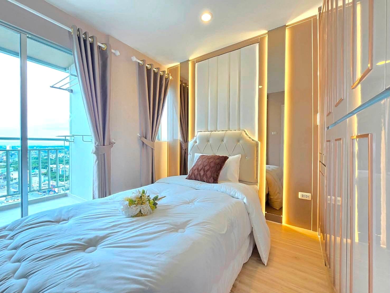 Lumpin_NorthPattaya_Sukhumvit_Dlc643_14 Luxurious white tufted bed in a bright modern bedroom with gold LED trim and mirrored wardrobe panels.