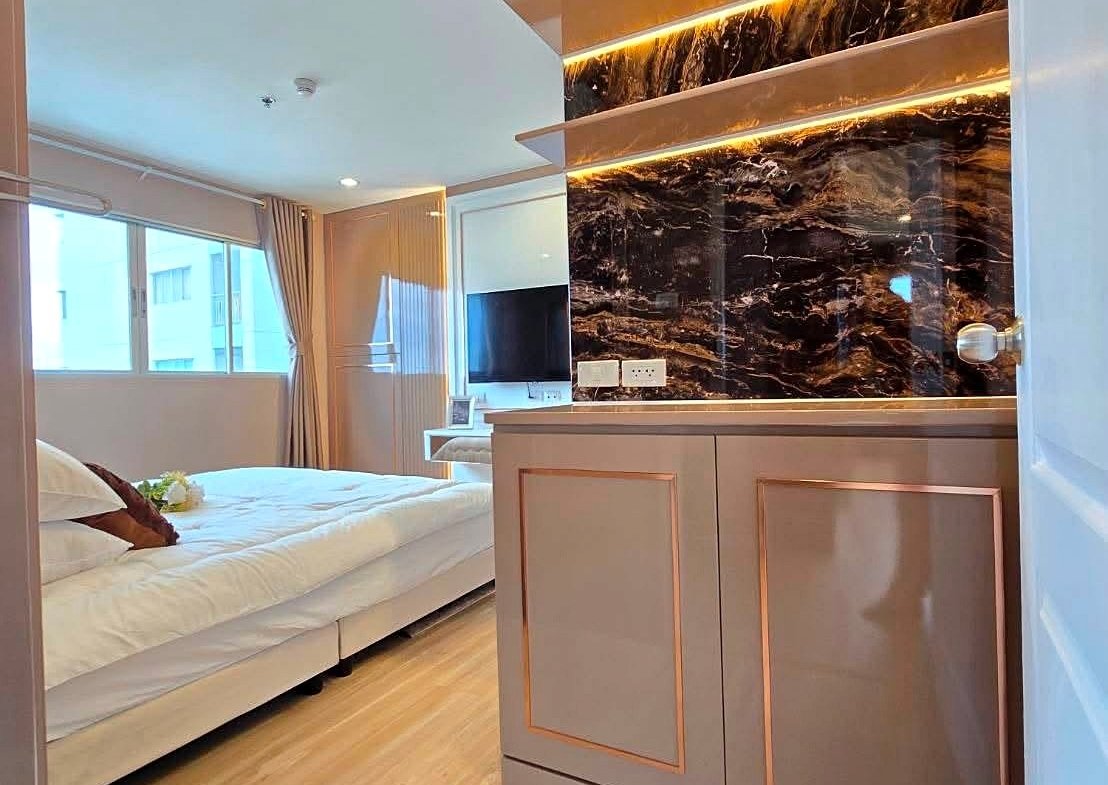 Modern hotel room: white bed on the left, wood floors, and an elegant copper-trimmed cabinet with a backlit black marble backsplash.