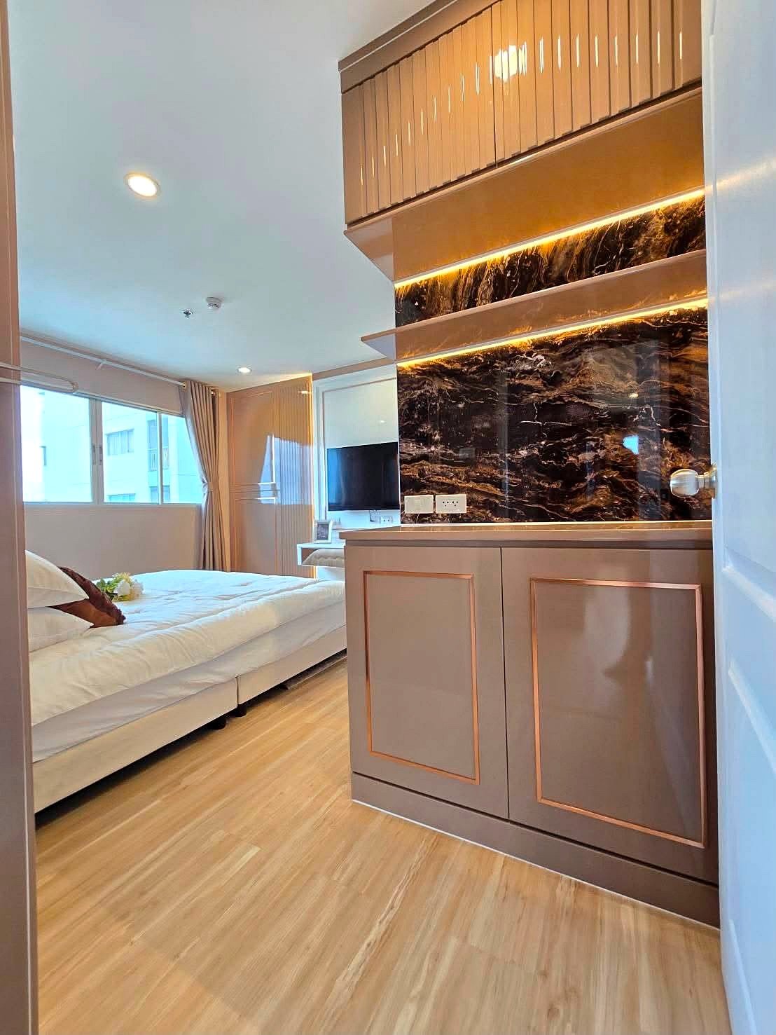 Lumpin_NorthPattaya_Sukhumvit_Dlc643_20 Modern hotel room: white bed on the left, wood floors, and an elegant copper-trimmed cabinet with a backlit black marble backsplash.