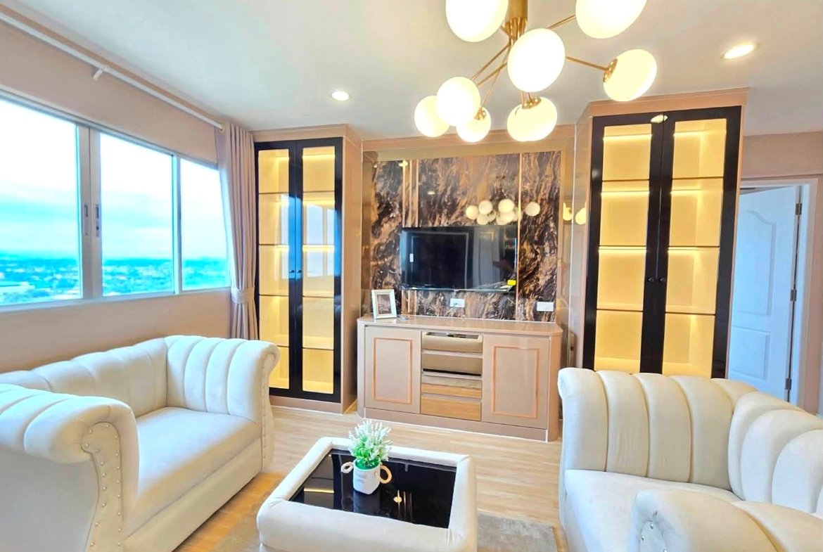 Bright living room with cream tufted sofas, a marble feature wall around the TV, and tall glass-front cabinets with warm backlighting beside a large window view of the city/landscape.