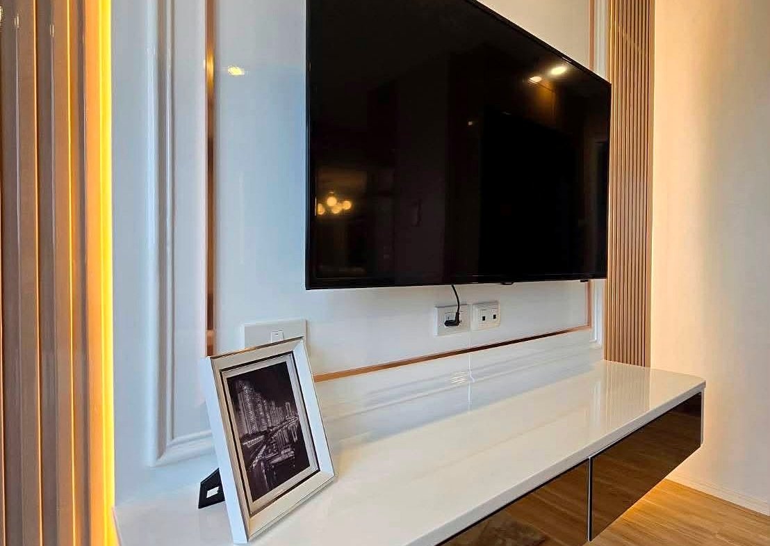 Modern living room entertainment wall with a mounted flat-screen TV above a glossy white console and a framed photo, accented by warm vertical LED lighting.