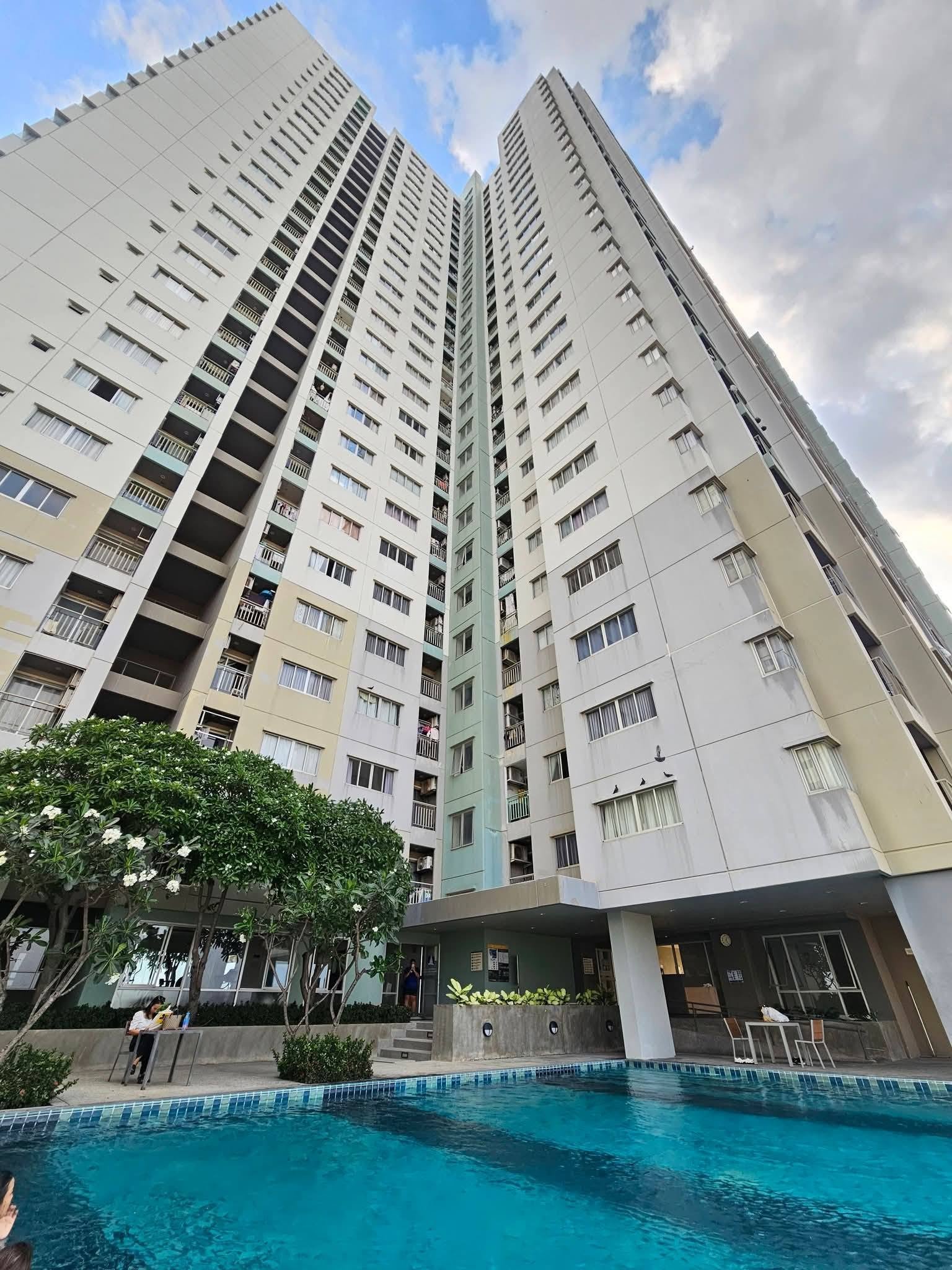 Lumpini_Condo_Town_North_Pattaya_Sukhumvit 1 Tall residential high-rise buildings surround a courtyard pool with blue water and greenery in the foreground.