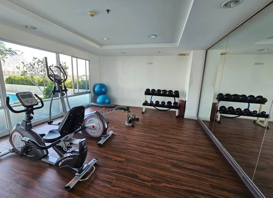 Small fitness room with cardio machines, a dumbbell rack, and two blue exercise balls by a windowed wall with a large mirror.