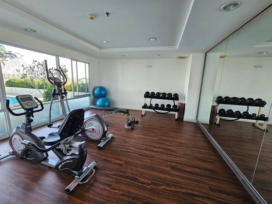 Lumpini_Condo_Town_North_Pattaya_Sukhumvit 10 Small fitness room with cardio machines, a dumbbell rack, and two blue exercise balls by a windowed wall with a large mirror.