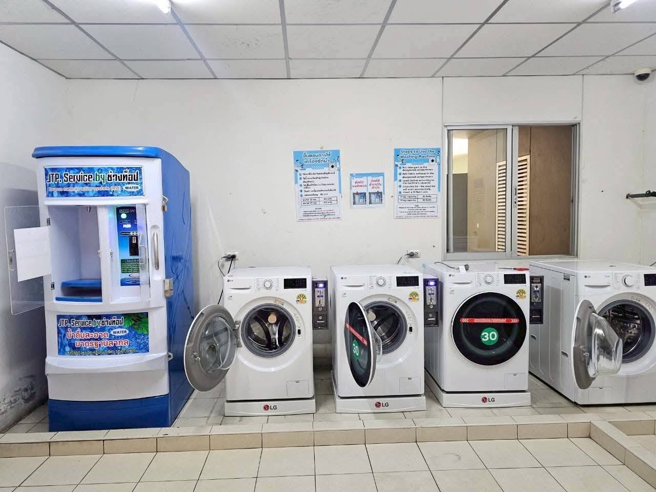 Lumpini_Condo_Town_North_Pattaya_Sukhumvit 3 Row of LG front-loading washing machines in a laundromat, doors open, with a blue water vending machine on the left.