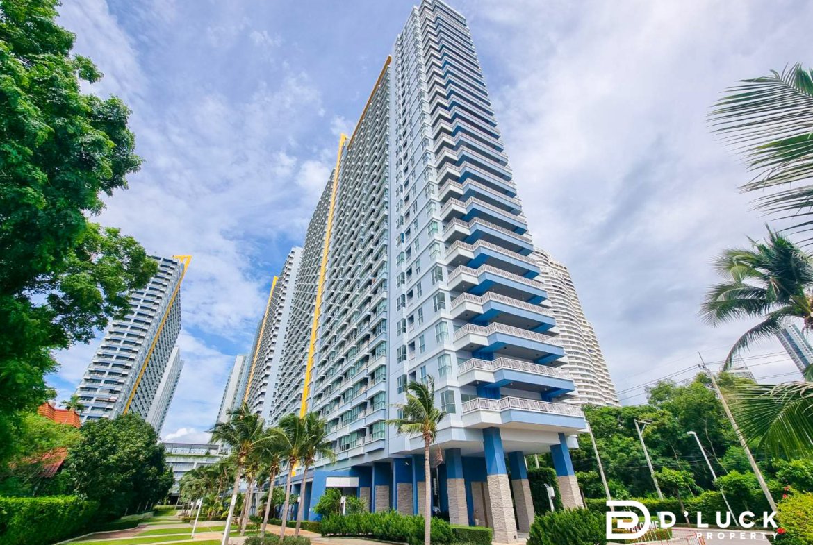 Tall modern condo tower with blue balconies, surrounded by palm trees and manicured landscaping under a blue sky.
