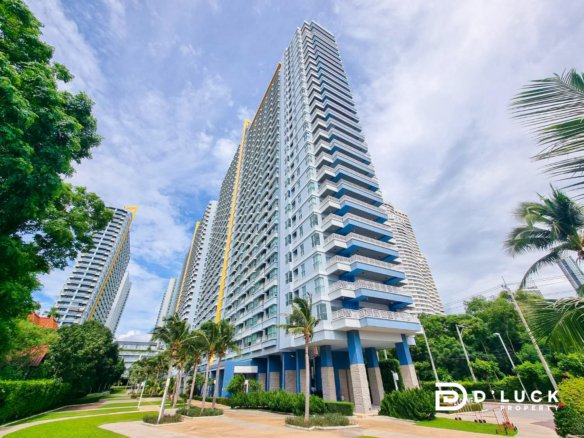 Tall modern condo tower with blue balconies surrounded by palm trees and manicured landscaping under a blue sky