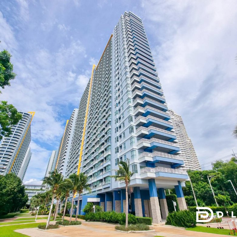 Tall modern condo tower with blue balconies surrounded by palm trees and manicured landscaping under a blue sky
