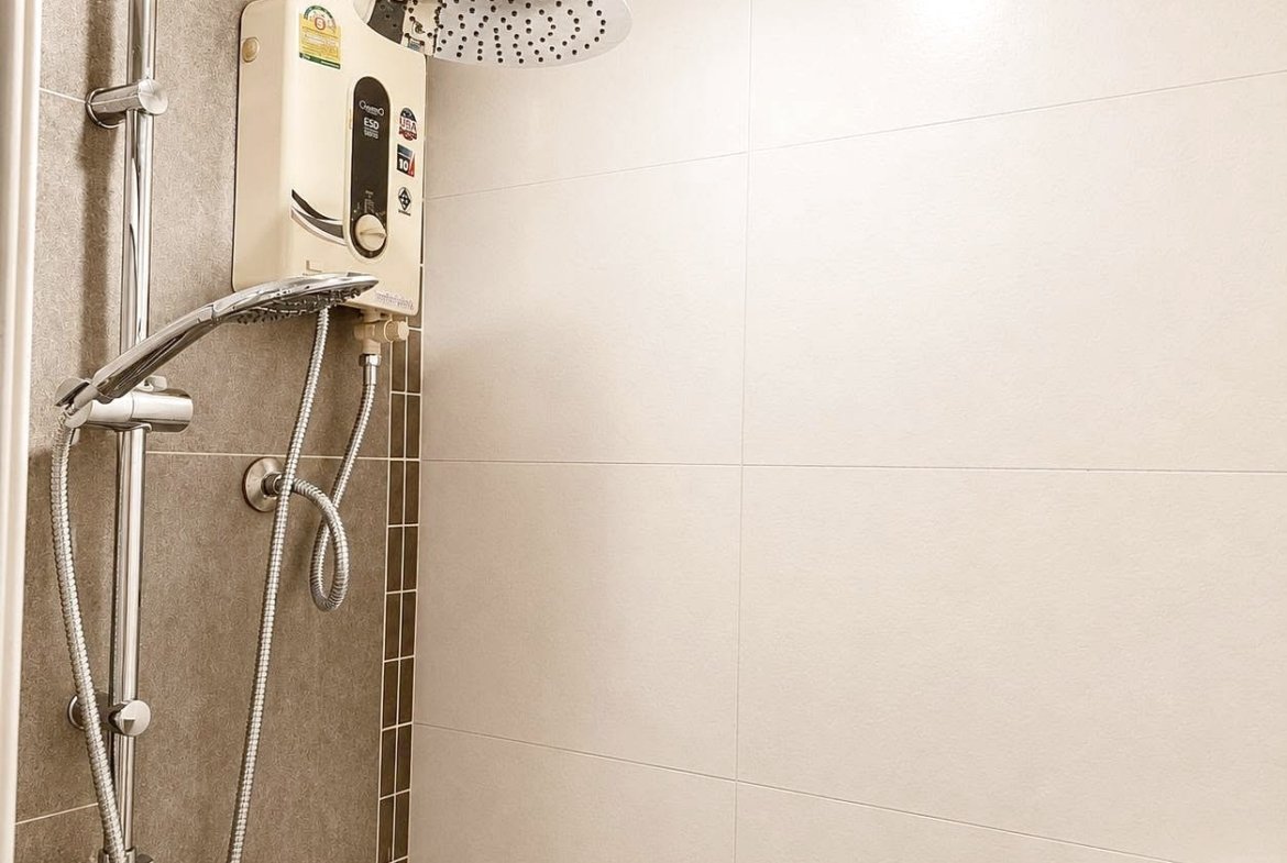 Shower area in a tiled bathroom featuring a ceiling rain shower, a handheld shower on a chrome rail, and a wall-mounted electric water heater unit behind the shower panel