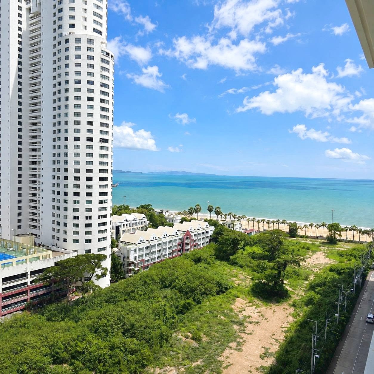 Lumpini_Park_Beach_Sale_Dlc650_15 Tall white apartment tower beside a sandy beach and turquoise sea with palm-lined shore.