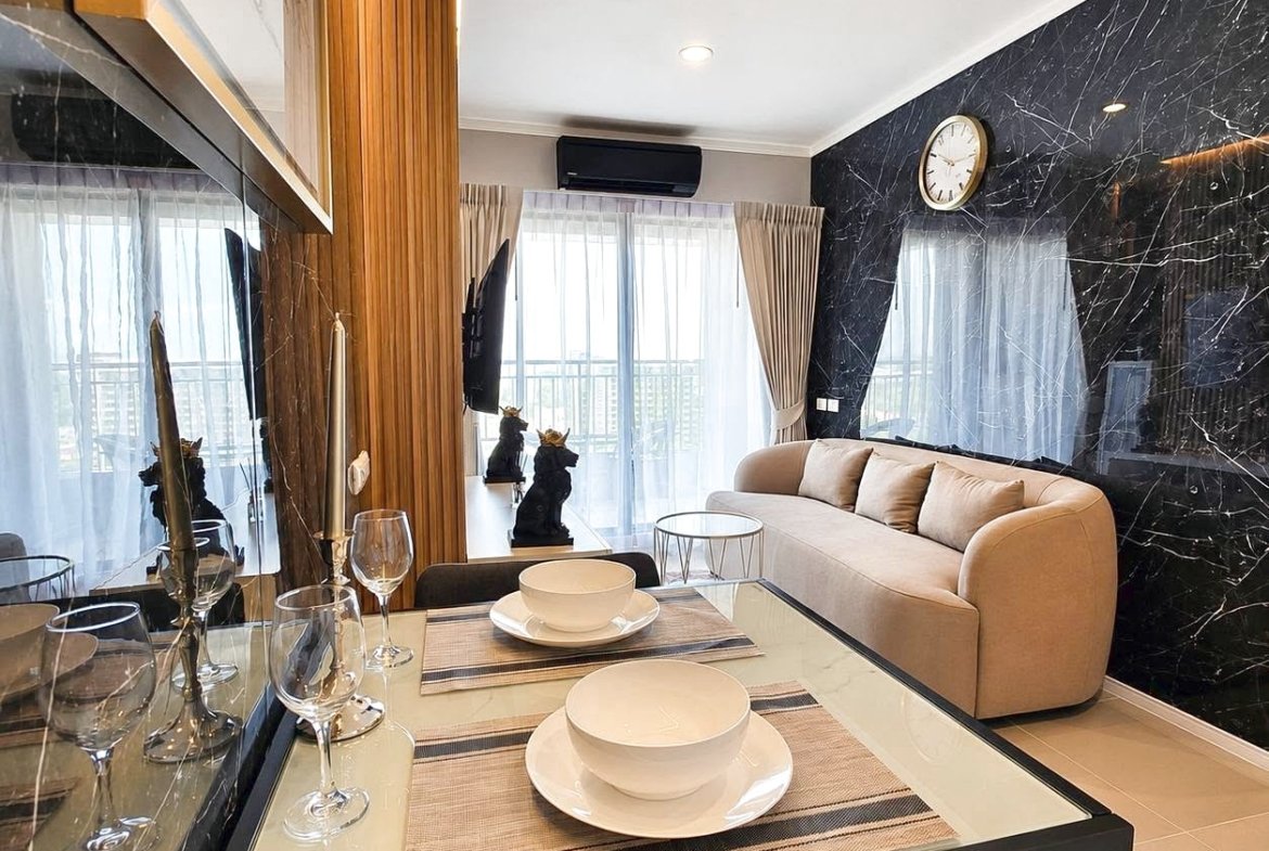 Contemporary living and dining area: glass table set for two with bowls and wine glasses, beige sofa, and a black marble accent wall.