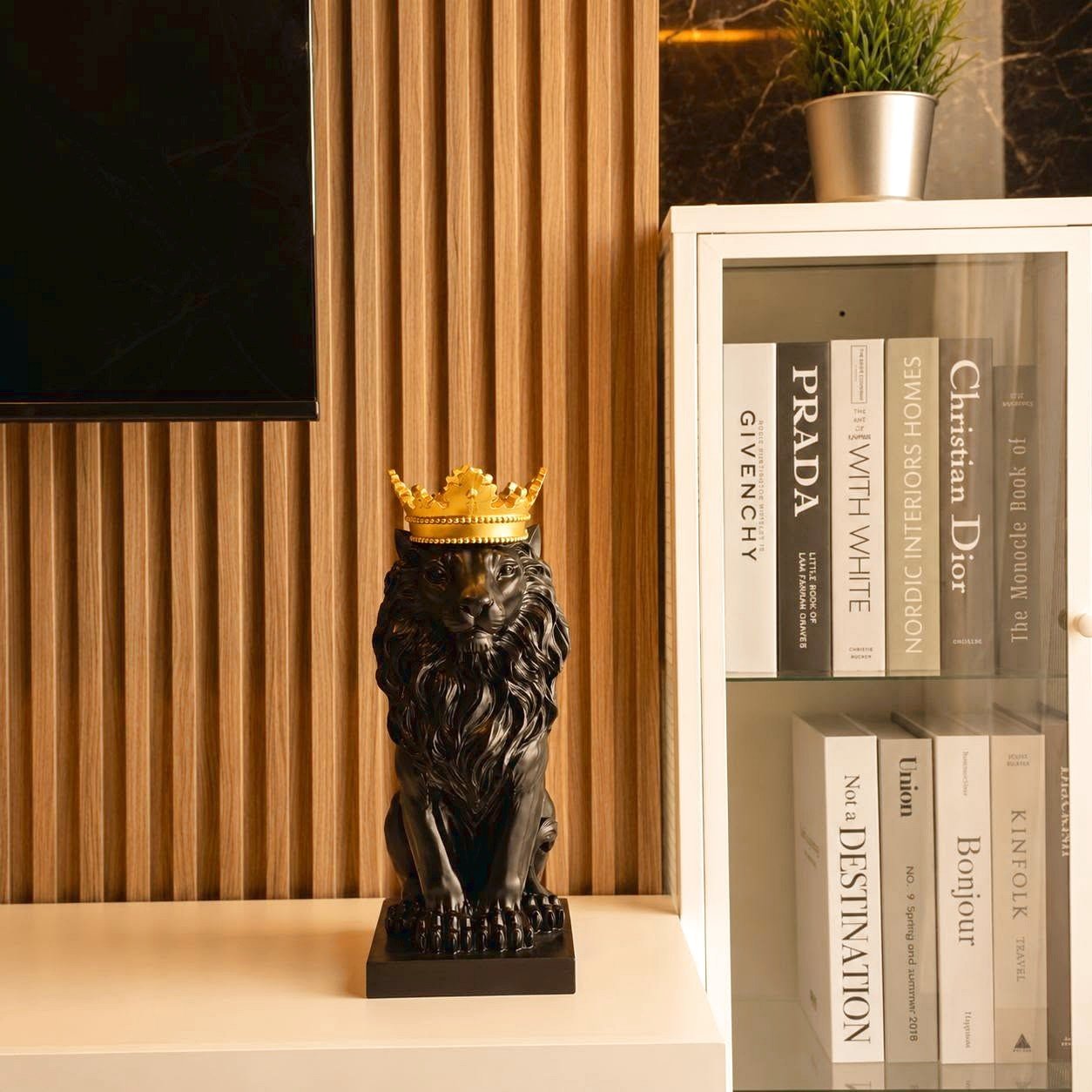 Lumpini_Park_Beach_Sale_Dlc650_8 Decorative black lion statue wearing a gold crown on a white shelf beside a glass-front bookcase with neutral books and a plant nearby.