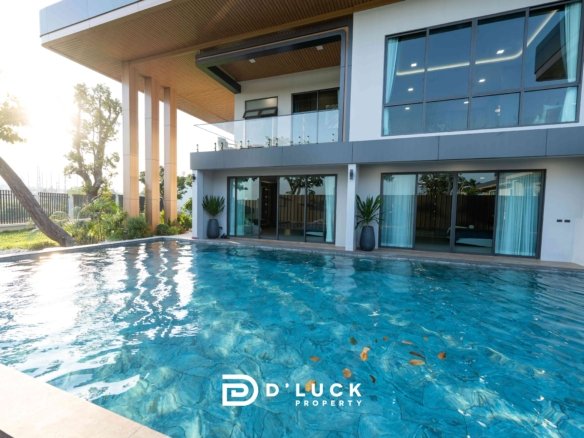 Modern two-story house with glass balcony, large windows, and a blue swimming pool in the foreground; D Luck Property logo visible at bottom.