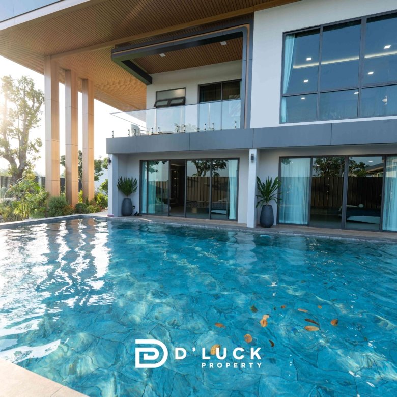 Modern two story house with glass balcony large windows and a blue swimming pool in the foreground D Luck Property logo visible at bottom