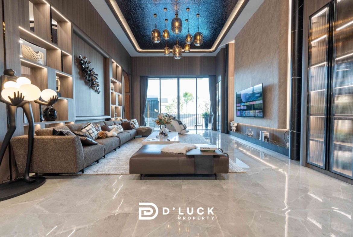 Luxurious modern living room with a gray sectional, built-in shelving, and a blue-lit ceiling chandelier area view outside through glass doors, logo at bottom says D'Luck Property.