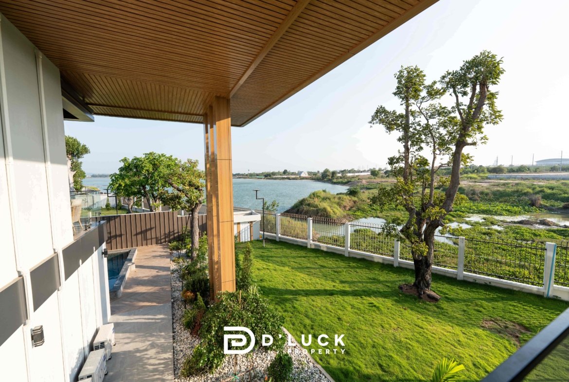 Modern home exterior with a wooden slatted overhang, patio area, and a lawn overlooking a body of water; Duck Property logo at bottom.