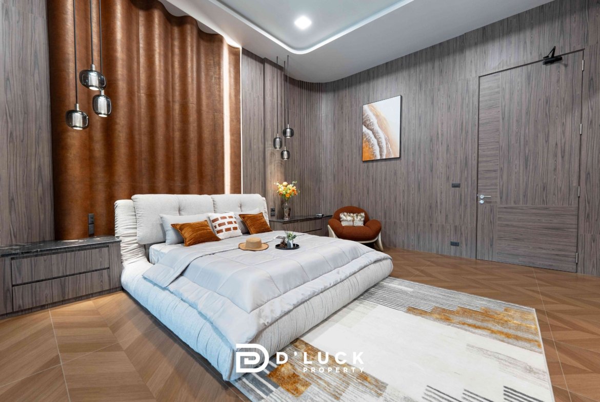 Modern bedroom with gray wood-paneled walls, a brown leather curtain, and pendant lights over a plush gray bed with orange pillows.