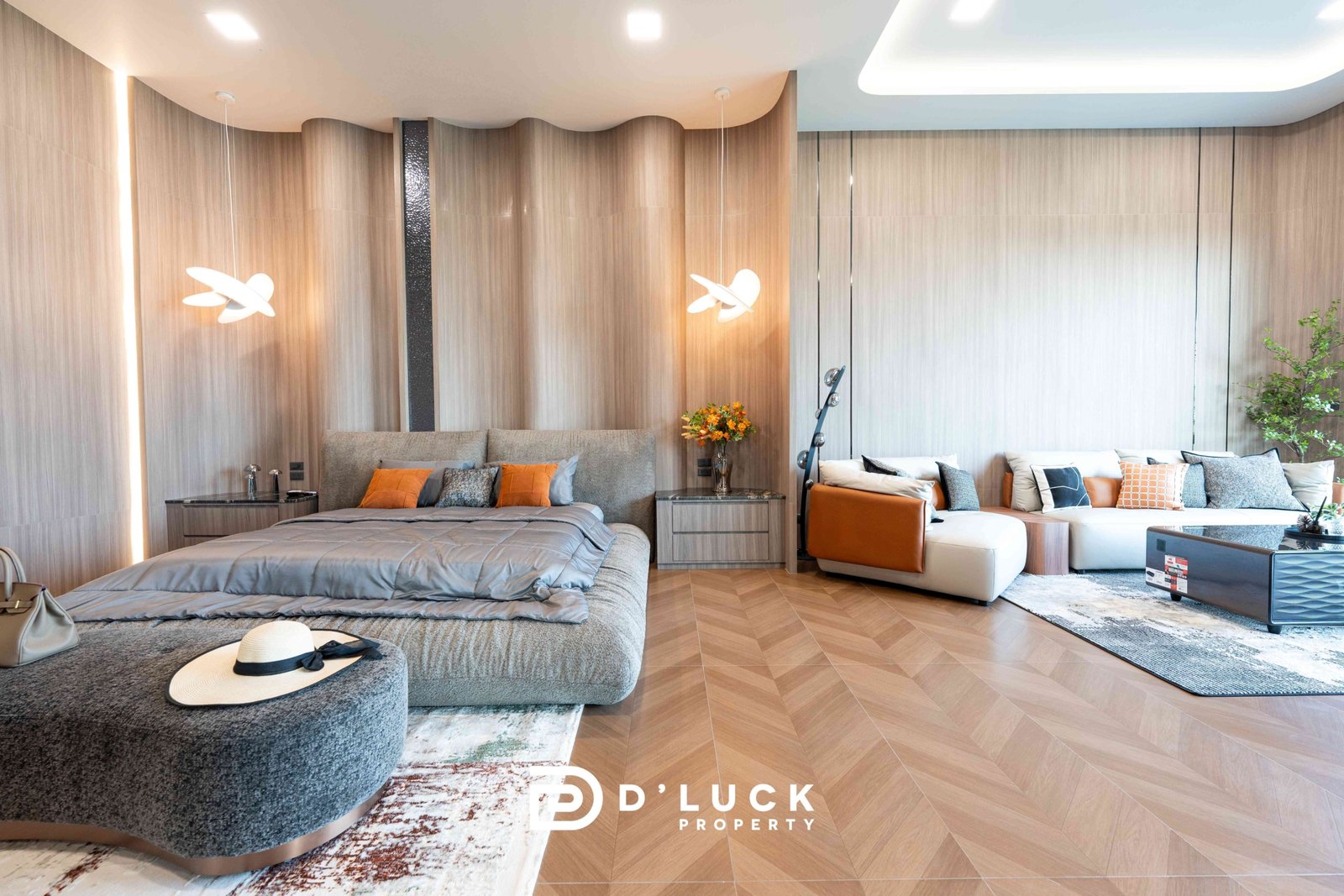 M-Mountian-M3 26 Luxurious hotel suite living area with a gray upholstered bed, orange pillows, a matching gray sofa, and sculptural white pendant lights against wood-paneled walls.