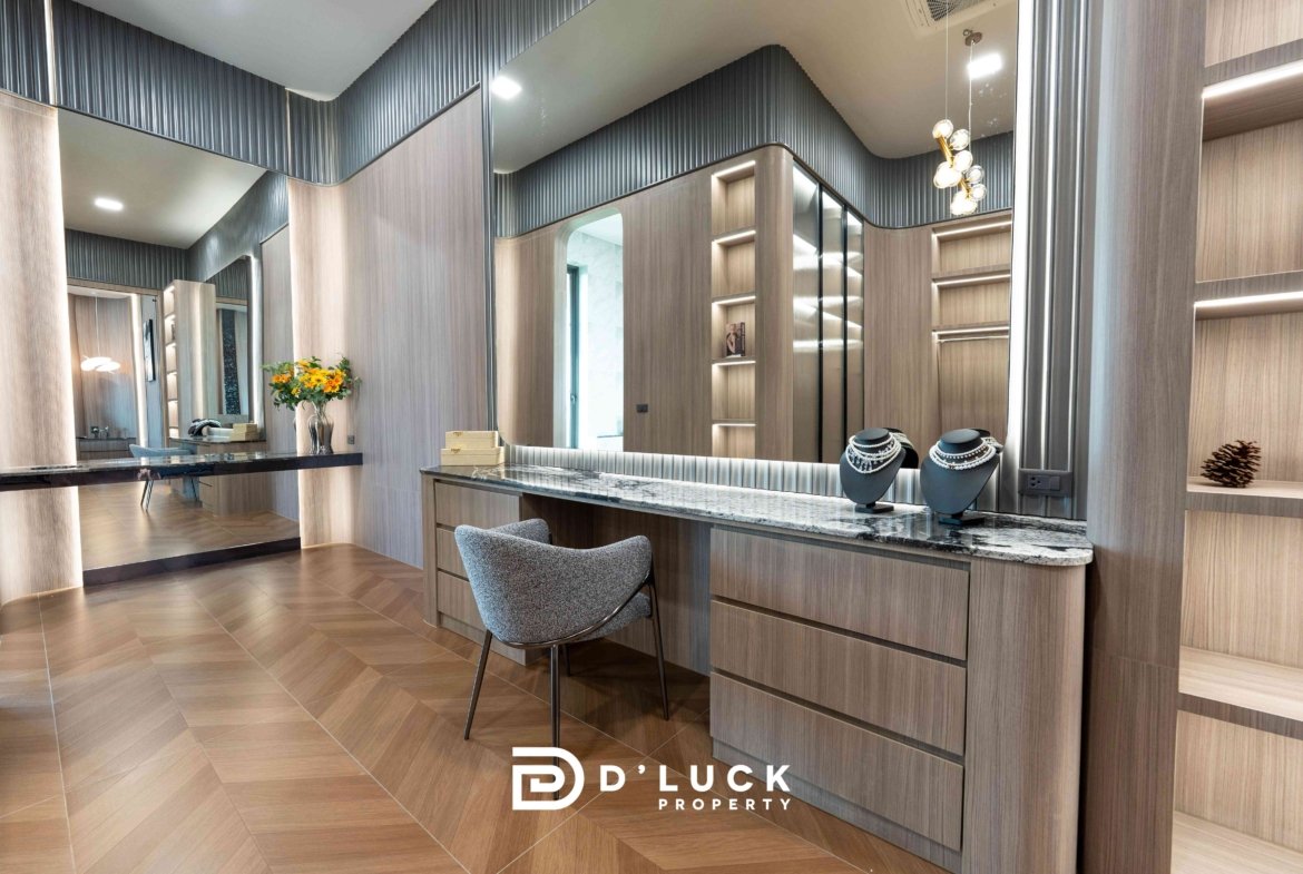 Luxurious jewelry showroom interior with wood display cabinets, marble counter, and mirrored walls displaying necklaces and lights. The 'D'LUCK Property' logo appears at the bottom.