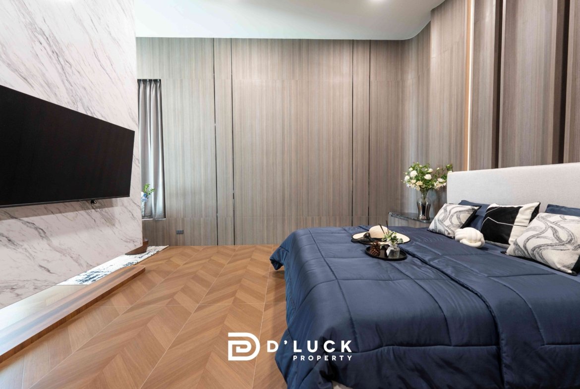 Modern hotel-style bedroom with a blue comforter, gray wood wall panels, and a large wall-mounted TV on a marble accent wall.