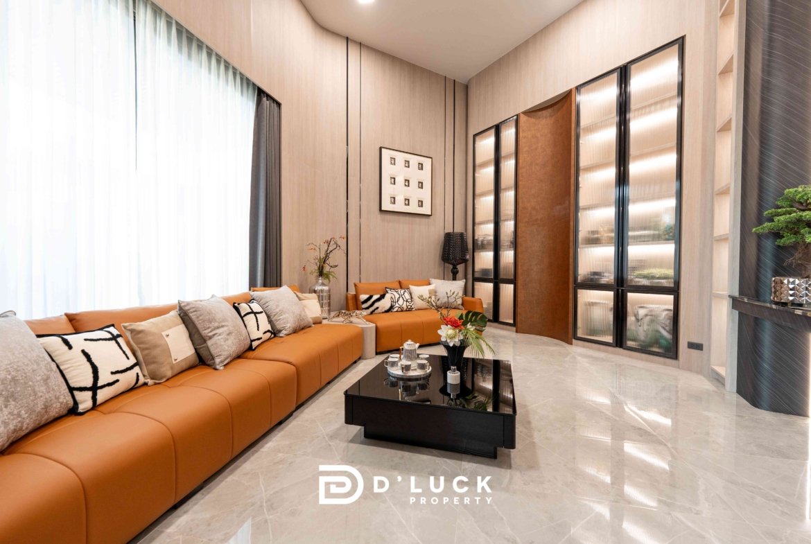 Modern living room with an orange sectional sofa, neutral cushions, and a glass coffee table in a bright showroom setting, featuring wall panels and tall glass-front cabinets.