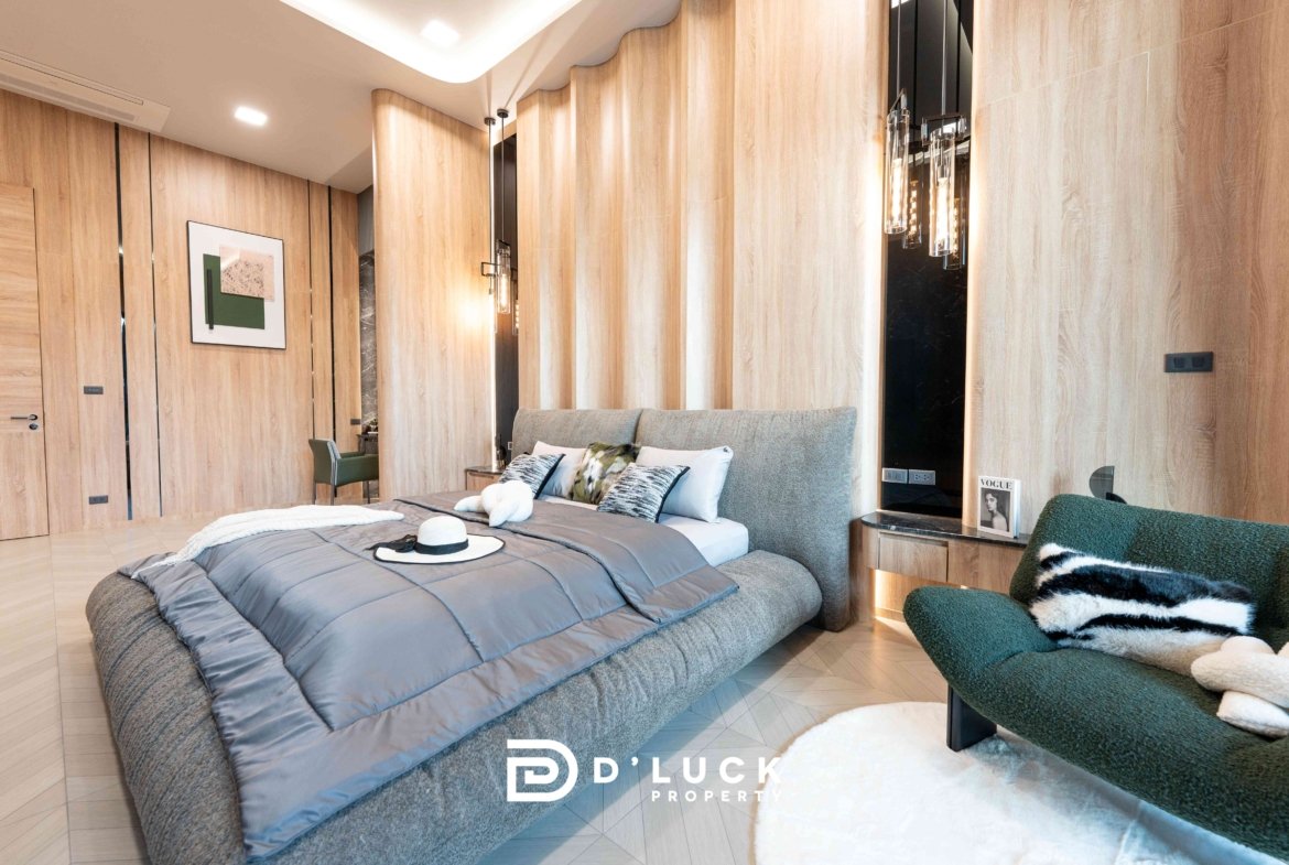 Luxurious bedroom with wood-paneled walls, gray upholstered bed, and green chairs; hat on bed and Vogue magazine on the nightstand.