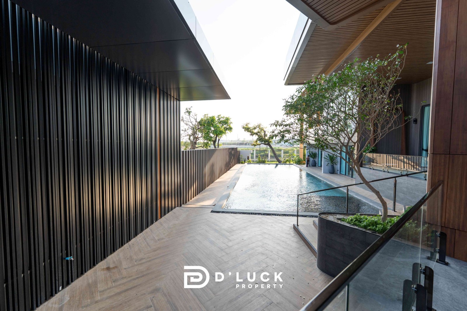 M-Mountian-M3 93 Contemporary outdoor atrium between a dark vertical-slat wall and a wooden facade, with a narrow water feature and trees in the background.