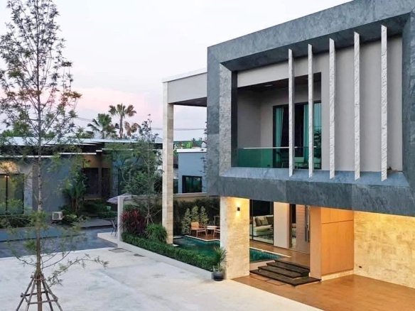 Modern two story house with a gray stone frame glass balcony and warm lit ground level living area beside a pool