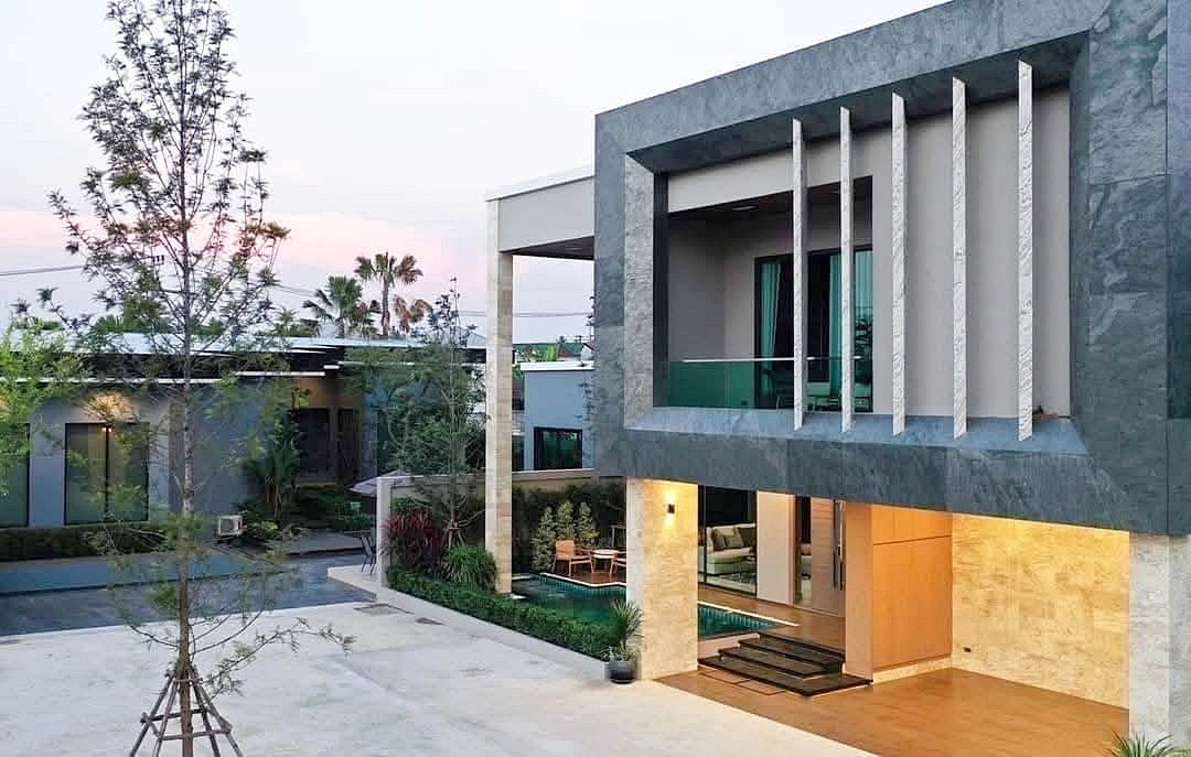 Modern two story house with a gray stone frame glass balcony and warm lit ground level living area beside a pool