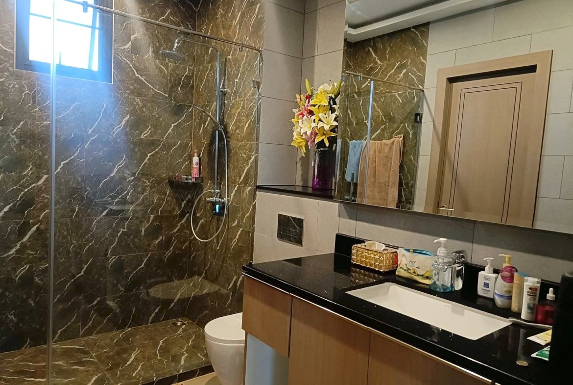 Modern bathroom with dark marble walls, glass shower enclosure, and a black countertop vanity; colorful flower arrangement on the counter.