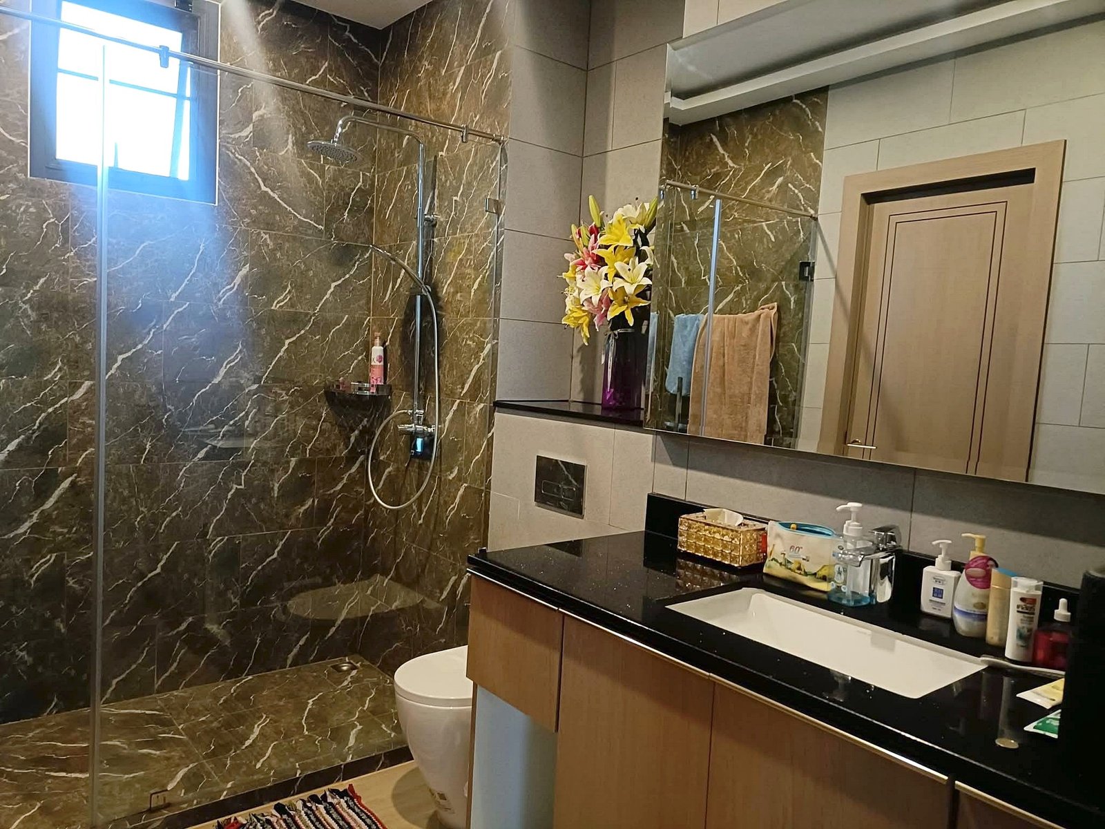 Modern bathroom with dark marble walls, glass shower enclosure, and a black countertop vanity; colorful flower arrangement on the counter.