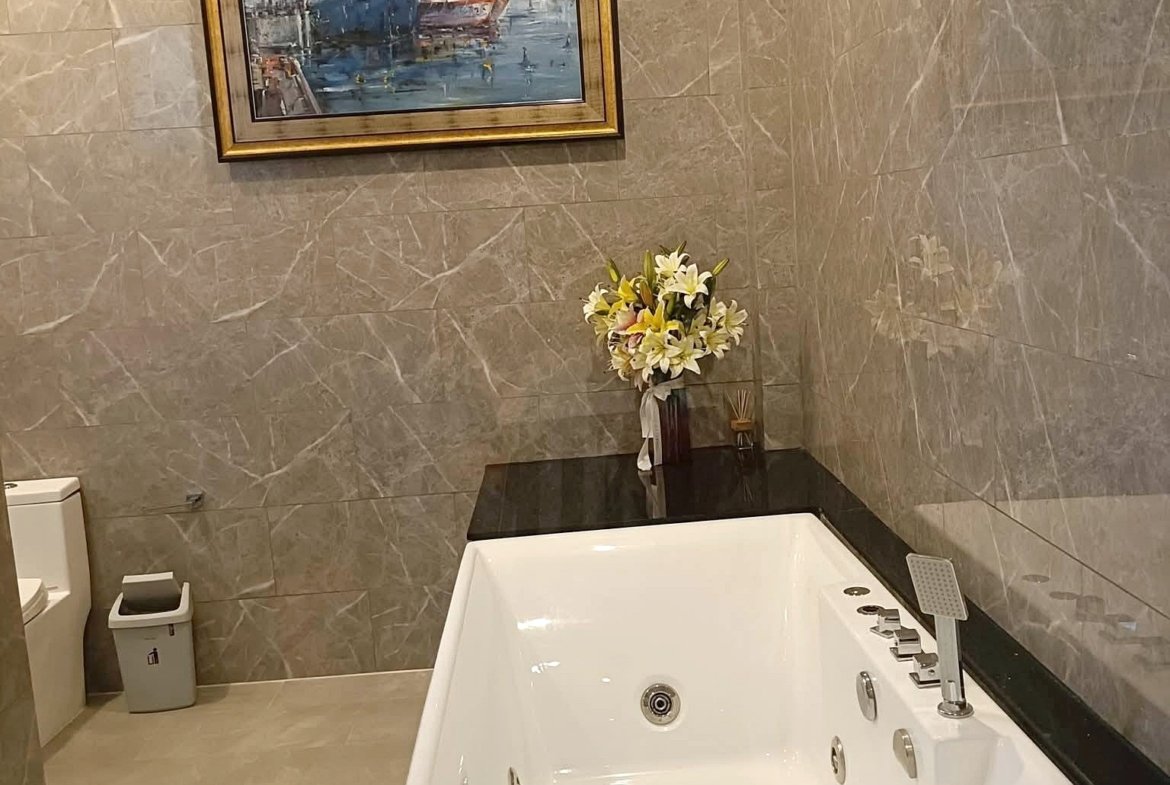 Luxurious bathroom with a white whirlpool tub, black countertop, and a framed maritime painting on marble walls, plus a floral bouquet on the counter.