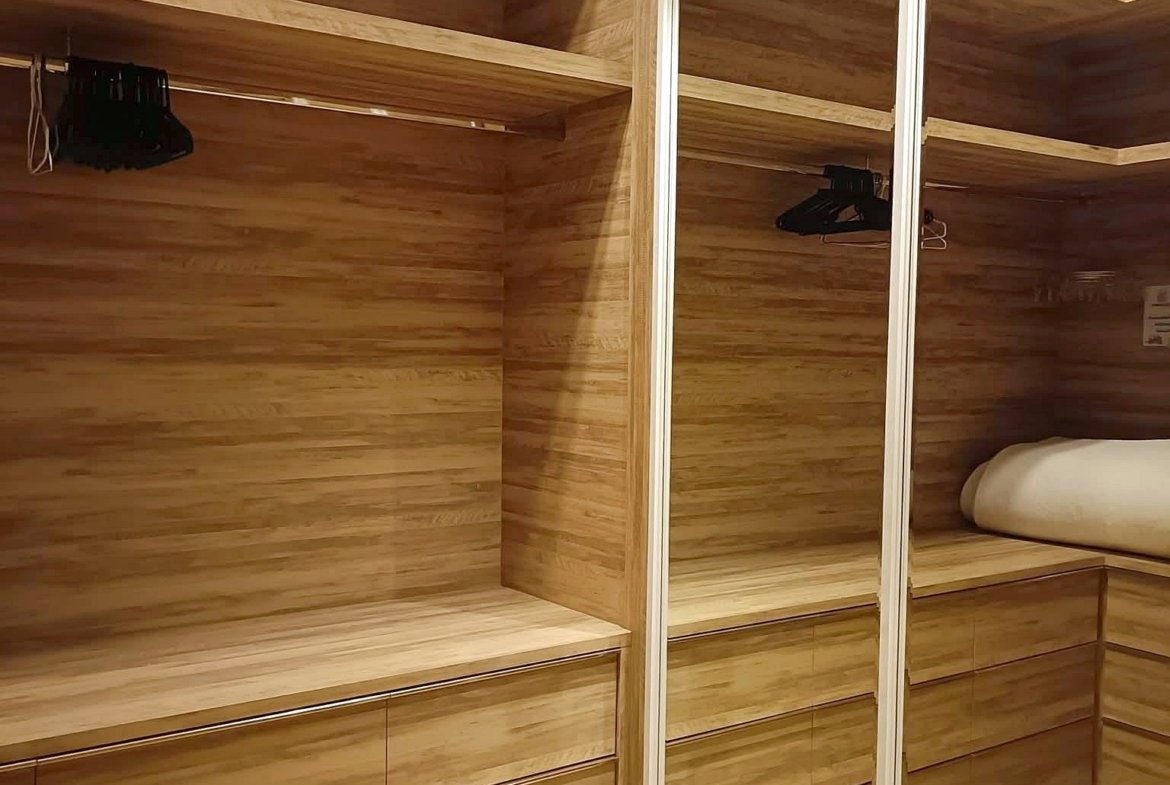 Walk-in closet with warm wood cabinetry, multiple shelves and drawers, and mirrored sliding doors.