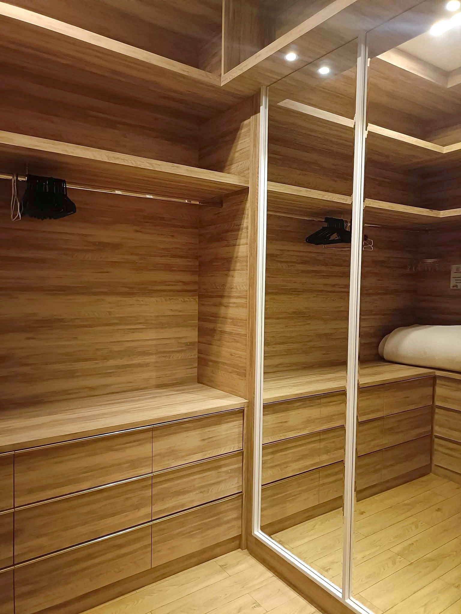 Walk-in closet with warm wood cabinetry, multiple shelves and drawers, and mirrored sliding doors.