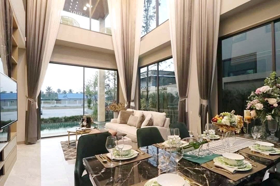 Open-plan living and dining area with tall glass walls, neutral curtains, and a marble dining table set for six, plus a beige sofa and greenery outside.