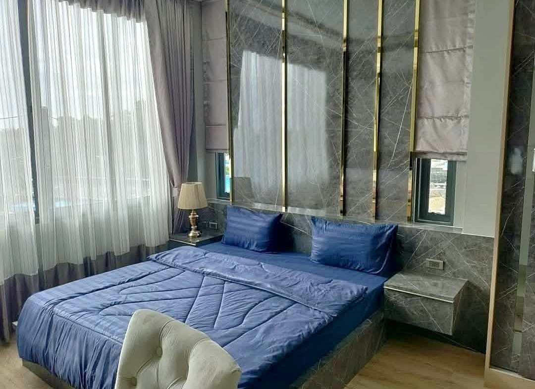 Modern hotel-style bedroom with a blue duvet, two matching blue pillows, and marble wall panels behind the bed.